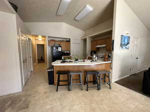 Kitchen featuring a kitchen breakfast bar, light tile patterned flooring, sink, vaulted ceiling, and kitchen peninsula