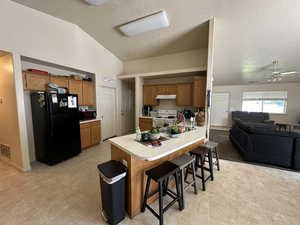 Kitchen with tile patterned floors, vaulted ceiling, and a breakfast bar and decorative shelf above