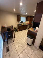 Kitchen featuring a textured ceiling, dishwasher, dark brown cabinetry, light tile floors, and sink