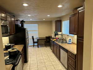 Kitchen featuring black/stainless steel appliances, a textured ceiling, tile floor, dark brown custom cabinets