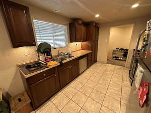 Kitchen with sink, dark brown cabinets, light tile flooring, and stainless steel dishwasher