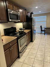 Kitchen featuring black/stainless steel appliances, a textured ceiling, tile floor, dark brown custom cabinets