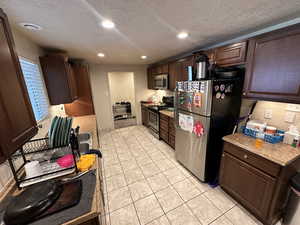 Kitchen featuring appliances with stainless steel finishes, dark brown cabinetry, a textured ceiling, and light tile patterned floors