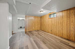 Basement with wood walls, light hardwood / wood-style flooring, and a textured ceiling