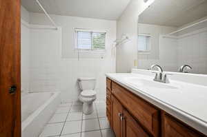 Full bathroom featuring toilet, tile patterned floors, tiled shower / bath, tile walls, and vanity