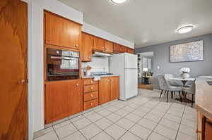 Kitchen with black oven, light tile patterned floors, and white fridge