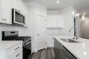 Kitchen with stainless steel appliances, dark wood-type flooring, sink, pendant lighting, and white cabinetry