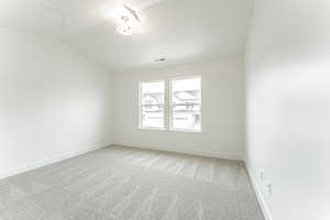 Spare room featuring light carpet, a textured ceiling, lofted ceiling, baseboards, and visible vents