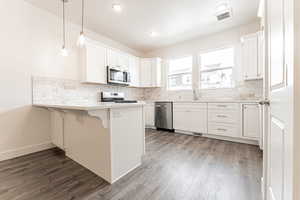 Kitchen with wood finished floors, a peninsula, stainless steel appliances, visible vents, and decorative backsplash