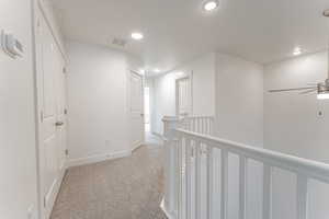 Hall with an upstairs landing, light carpet, baseboards, visible vents, and recessed lighting