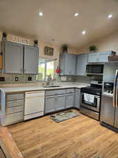 Kitchen with appliances with stainless steel finishes, light hardwood / wood-style flooring, gray cabinets, and sink