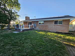 Rear view of house with a wooden deck, solar panels, and a yard