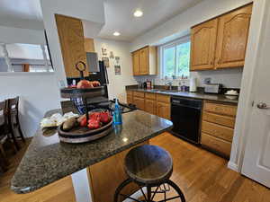 Kitchen featuring light hardwood / wood-style flooring, a kitchen bar, black dishwasher, dark stone countertops, and sink