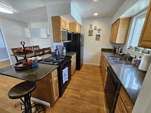 Kitchen featuring light wood-type flooring, sink, black appliances, and dark stone counters