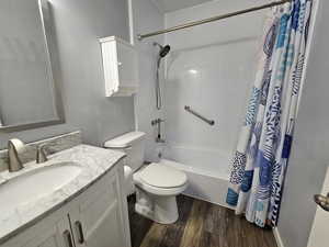 Full bathroom with hardwood / wood-style floors, shower / tub combo with curtain, vanity, and toilet