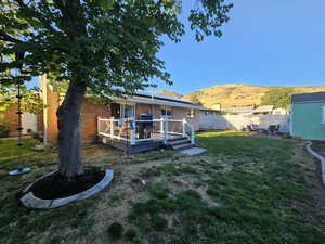 Back of house with a deck with mountain view and a lawn