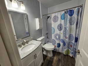 Full bathroom with wood-type flooring, vanity, toilet, and shower / bath combination with curtain