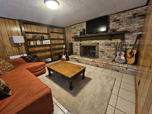 Living room featuring light tile patterned floors, wood walls, a fireplace, and brick wall