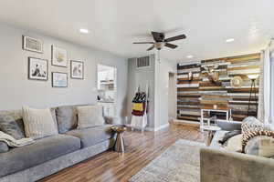 Living room with ceiling fan, wood-type flooring, and wooden walls