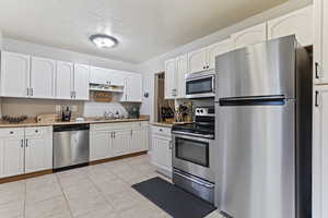 Kitchen with appliances with stainless steel finishes, light stone countertops, white cabinets, light tile patterned floors, and sink