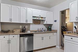 Kitchen with white cabinetry, sink, light tile patterned floors, and stainless steel dishwasher