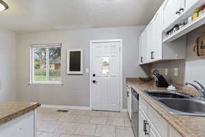 Kitchen featuring light tile patterned floors, sink, dishwasher, and white cabinetry