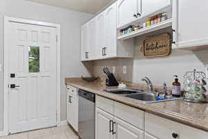 Kitchen with light tile patterned flooring, white cabinets, sink, and dishwasher