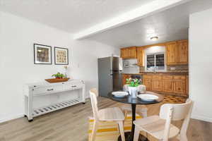 Dining area featuring beamed ceiling, a textured ceiling, and light wood-type flooring