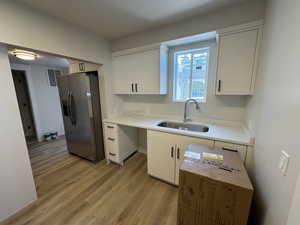 Kitchen featuring stainless steel fridge with ice dispenser, sink, white cabinets, and light hardwood / wood-style floors