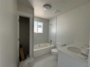 Full bathroom featuring a textured ceiling, tiled shower / bath, toilet, tile patterned floors, and vanity