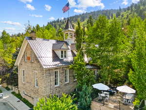 View of side of home featuring a standing seam roof, stone siding, a forest view, an attached garage, and a chimney