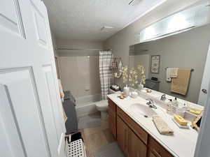 Full bathroom with a textured ceiling, toilet, tile patterned floors, shower / bathtub combination with curtain, and vanity