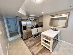 Kitchen with light hardwood / wood-style flooring, a textured ceiling, white cabinets, stainless steel fridge, and sink