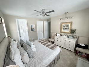 Main Floor Master Bedroom featuring ceiling fan, a walk in closet, a textured ceiling, and light colored carpet