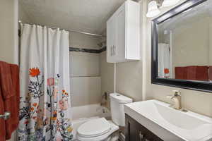 Full bathroom with a textured ceiling, shower / tub combo with curtain, toilet, and vanity