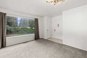 Carpeted front room featuring a notable chandelier, & big picture windows.