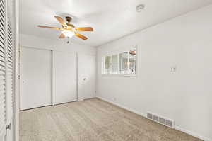 Unfurnished bedroom featuring a closet, light colored carpet, and ceiling fan