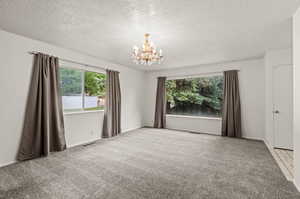 Empty room with light colored carpet, a chandelier, and a textured ceiling