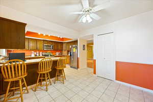 Kitchen with appliances with stainless steel finishes, a breakfast bar area, light tile patterned floors, and ceiling fan