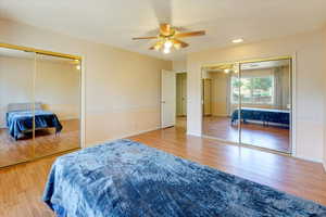 Bedroom with two closets, ceiling fan, and light hardwood / wood-style floors