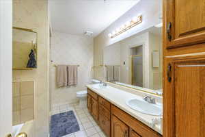 Bathroom featuring a shower with door, toilet, dual bowl vanity, and tile patterned floors