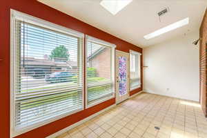 Unfurnished room with vaulted ceiling with skylight, light tile patterned flooring, and a healthy amount of sunlight