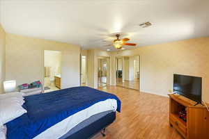 Bedroom with ensuite bath, light wood-type flooring, and ceiling fan