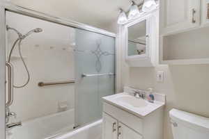 Full bathroom with enclosed tub / shower combo, toilet, and vanity