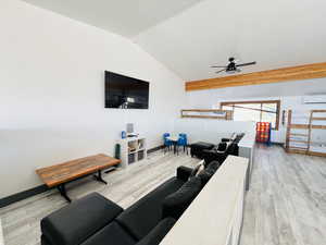 Living area with light wood-style flooring, a wall unit AC, baseboards, ceiling fan, and vaulted ceiling
