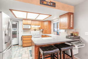 Kitchen with white appliances, a breakfast bar area, light tile patterned floors, sink, and kitchen peninsula