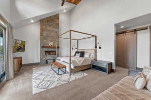 Carpeted bedroom with a tiled fireplace, high vaulted ceiling, a barn door, and tile walls