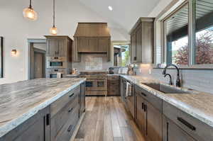 Kitchen with light wood-type flooring, decorative backsplash, stainless steel appliances, and decorative light fixtures