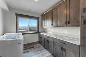 Clothes washing area with cabinets, light wood-type flooring, and washer and dryer