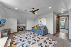 Living room with ceiling fan, a textured ceiling, light carpet, and vaulted ceiling